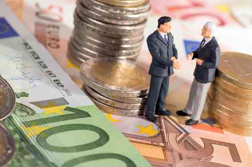 Zwei kleine Figuren stehend auf Geldscheine umringt von Münzen 